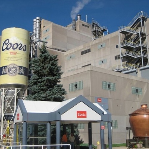 A large tank, painted like a Coors beer can, is at the entrance to the large brewery.