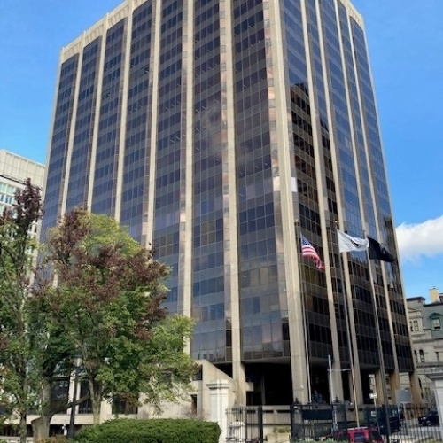 The American flag flies in front of a 22-story building with dark tinted windows. The McCormack Parking Garage was built at the base of the building.